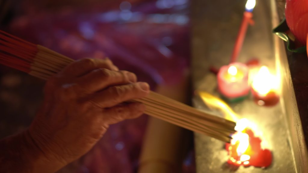 Close up of a hand holding Chinese incense to a flame